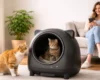 "A black, smart automatic litter box designed for multiple cats, with one cat using it while another watches, demonstrating its heavy-duty performance for multi-cat households in a modern living room."